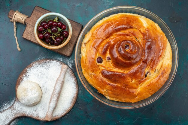 Top view of baked cherry cake with cherries inside along with flour dough and fresh sour cherries on dark desk, fruit bake cake sweet tea