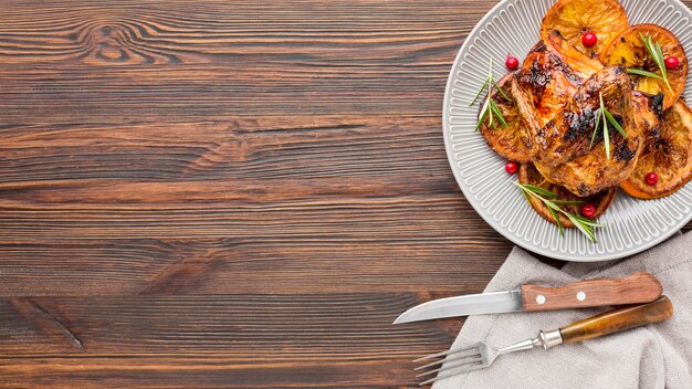 Top view baked chicken and orange slices on plate with cutlery and copy-space