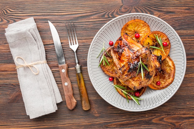 Top view baked chicken and orange slices on plate with cutlery and napkin