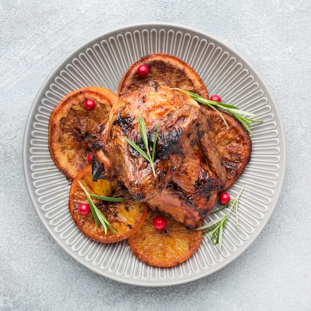 Top view baked chicken and orange slices on plate with herbs
