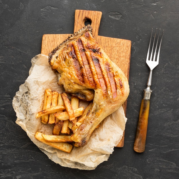 Вид сверху запеченный цыпленок и картофель на разделочной доске с вилкой