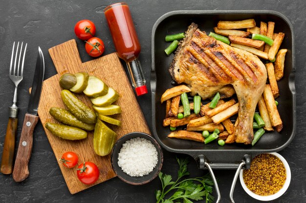 Top view baked chicken and potatoes in pan with pickles and tomatoes