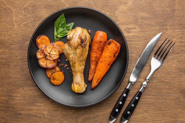 Top view baked chicken and veggies on plate with cutlery