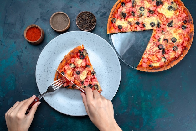 Vista dall'alto al forno deliziosa pizza con olive, salsicce e formaggio sulla scrivania blu.