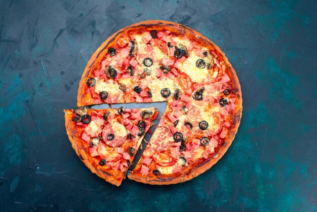 Вид сверху испеченная вкусная пицца с оливками, сосисками и сыром, нарезанным на синем столе.