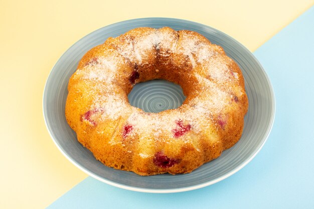 A top view baked fruit cake delicious round with red cherries inside and sugar powder inside round blue plate on pink and blue