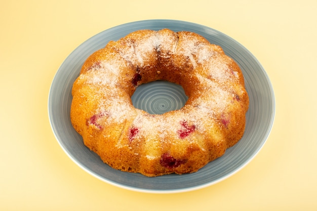 A top view baked fruit cake delicious round with red cherries inside and sugar powder inside round plate on yellow