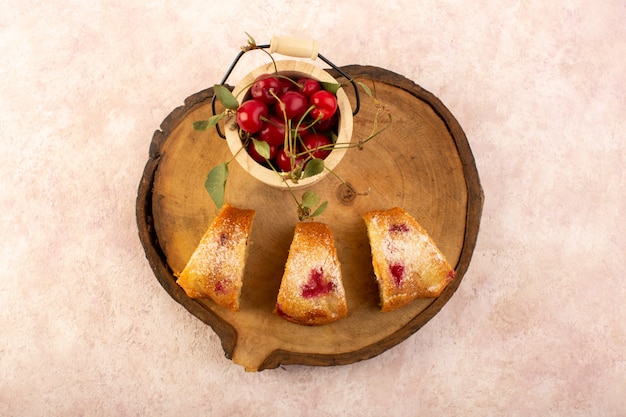 Foto gratuita una vista dall'alto torta di frutta al forno deliziosa affettata con ciliegie rosse all'interno e zucchero in polvere sulla scrivania in legno con ciliegie fresche sul rosa