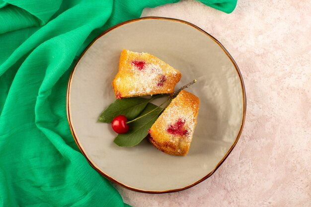 A top view baked fruit cake delicious slices with red cherries inside and sugar powder inside round grey plate on pink