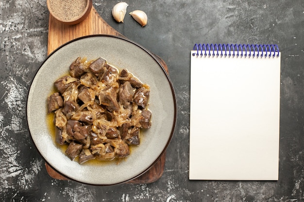 Top view baked liver and onion on plate black pepper on chopping board garlic notepad