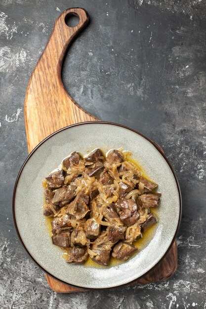 Top view baked liver with onion on grey round plate on chopping board