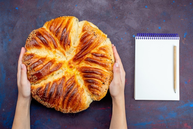 Top view baked pastry bun formed with notepad on dark background.