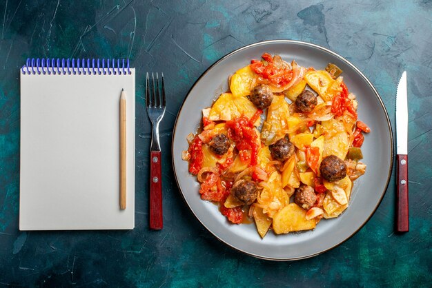 Top view baked potatoes with meatballs and vegetables inside plate on the dark-blue desk.