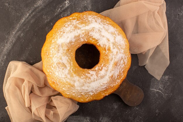 A top view baked round cake with sugar powder on the wooden desk