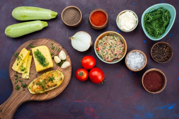 Бесплатное фото Вид сверху запеченные кабачки с сырной зеленью, фаршем и свежими овощами на темно-фиолетовом столе.