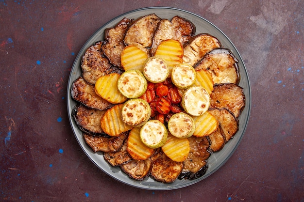 Top view baked vegetables potatoes and eggplants inside plate on dark space