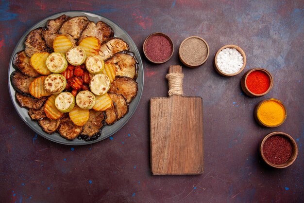Top view baked vegetables potatoes and eggplants with different seasonings on a dark space