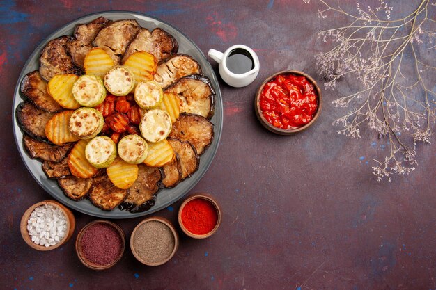 Top view baked vegetables potatoes and eggplants with different seasonings on a dark space