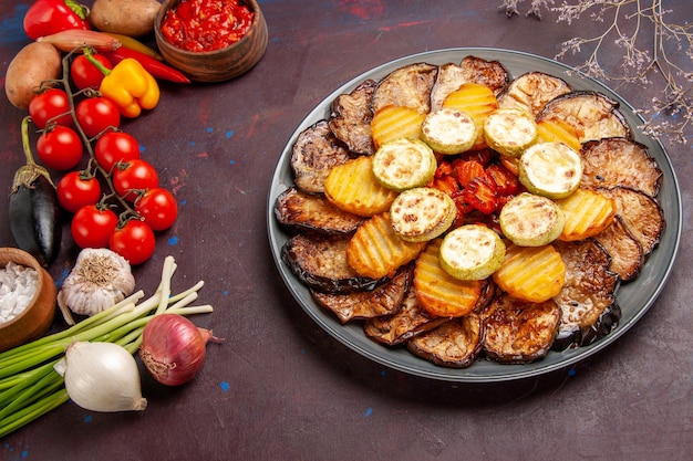 Top view baked vegetables potatoes and eggplants with fresh vegetables on dark space