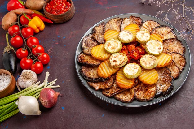 Top view baked vegetables potatoes and eggplants with fresh vegetables on dark space