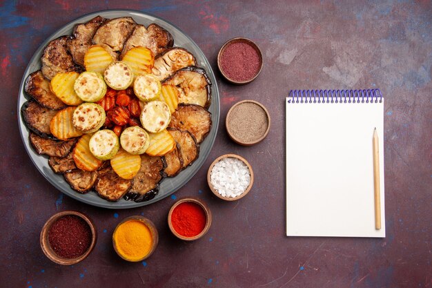 Top view baked vegetables potatoes and eggplants with seasonings on dark space