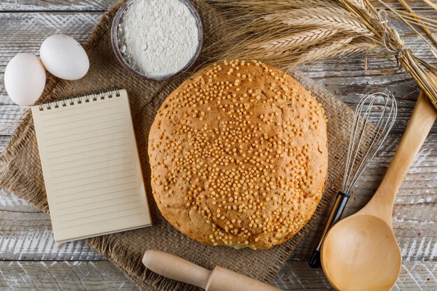 Top view bakery product with eggs, rolling pin, notepad, spoon, flour on wooden surface. horizontal
