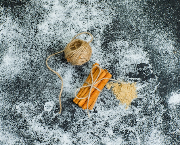 Top view a ball of rope tied to dry cinnamon on gray textured surface. horizontal