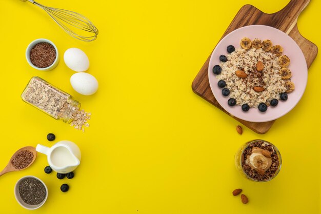 Top view of banana blackthorn almond flax oatmeal in plate on cutting board with banana walnut almond peanut butter smoothie in glass and ingredients for making them on yellow background