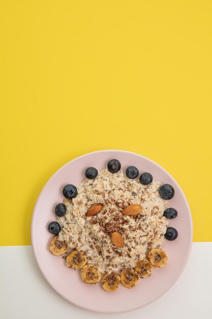 Top view of banana blackthorn almond flax oatmeal in plate on white and yellow background with copy space