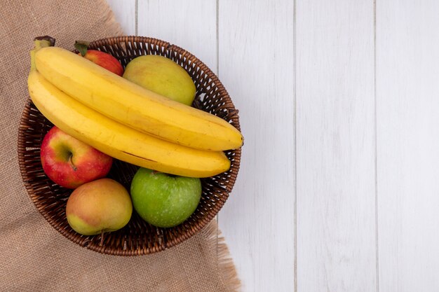 Top view of bananas with apples in a basket on a white surface