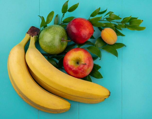Вид сверху бананов с цветными яблоками и персиком с абрикосом на ветвях на бирюзовой поверхности