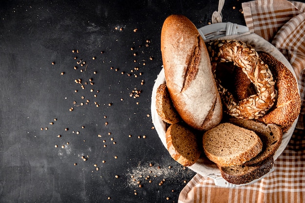 Top view of basket full of breads as baguette bagel rye with sunflower seeds on black surface