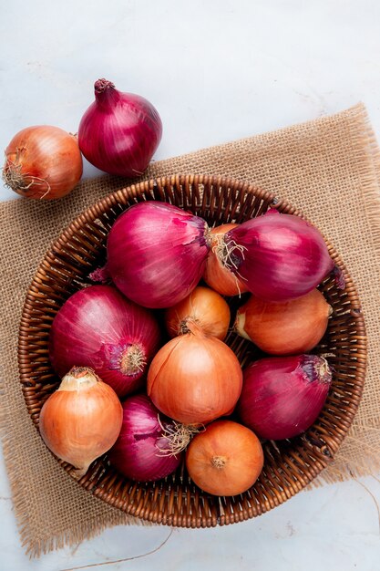 Top view of basket full of onions on sackcloth on white background