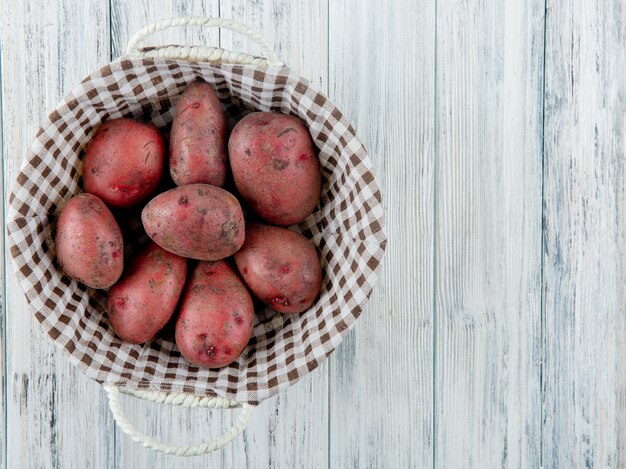 Top view of basket full of potatoes on left side and wooden background with copy space