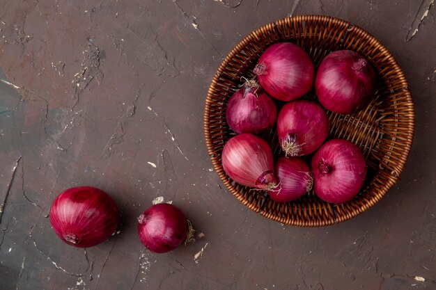 Top view of basket full of red onions on maroon background with copy space