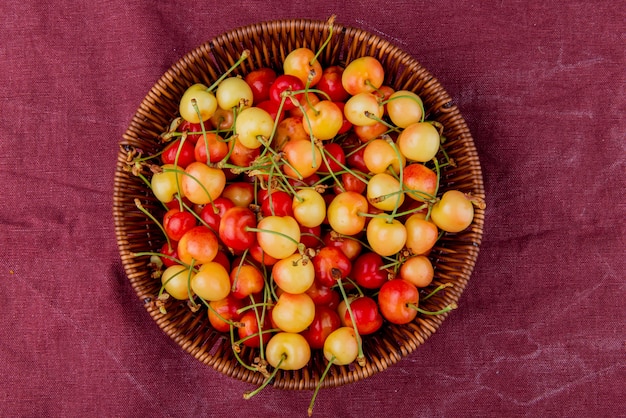 Free photo top view of basket full of yellow and red cherries on bordo cloth surface