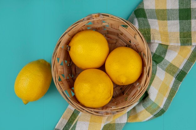 Top view of basket of lemons on plaid cloth on blue background