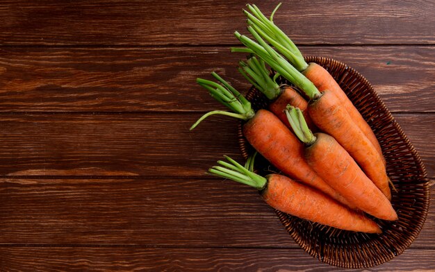 Top view of basket plate with carrots on wooden background with copy space