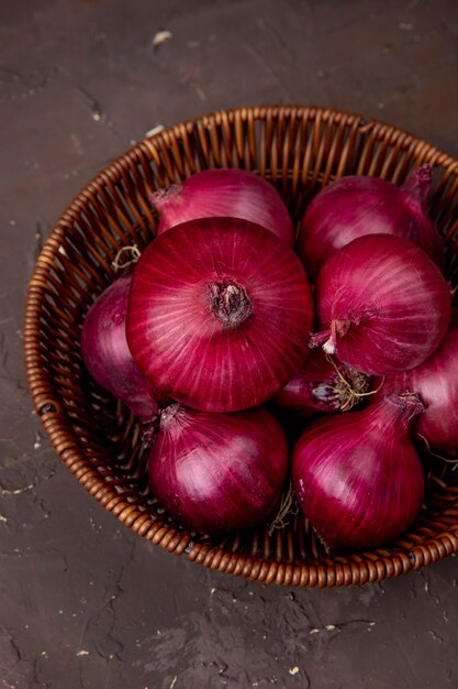 Top view of basket of red onions on maroon background