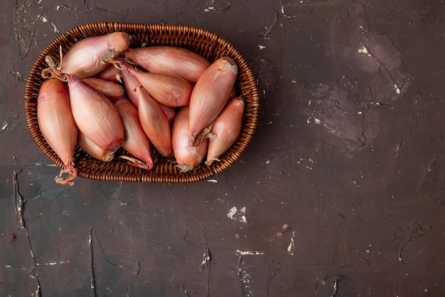 Top view of basket of shallots on left side and maroon background with copy space