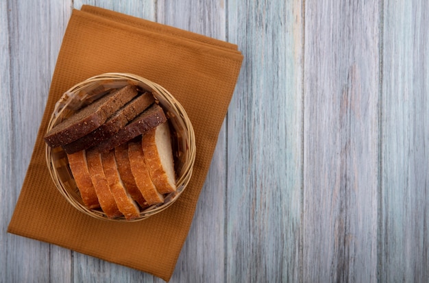 Вид сверху на корзину нарезанного хлеба в виде ржаного и хрустящего хлеба на ткани на деревянном фоне с копией пространства