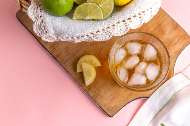 Top view of basket with citruses lemons and limes inside with iced drink on pink surface