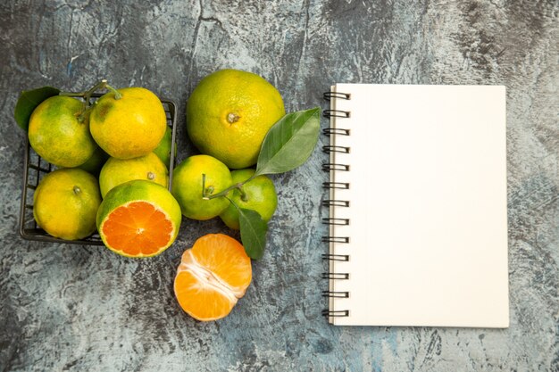 Top view of basket with fresh green tangerines cut in half and peeled tangerine next to notebook on gray background