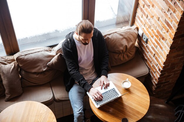 Вид сверху Бородатый мужчина, используя ноутбук в кафе
