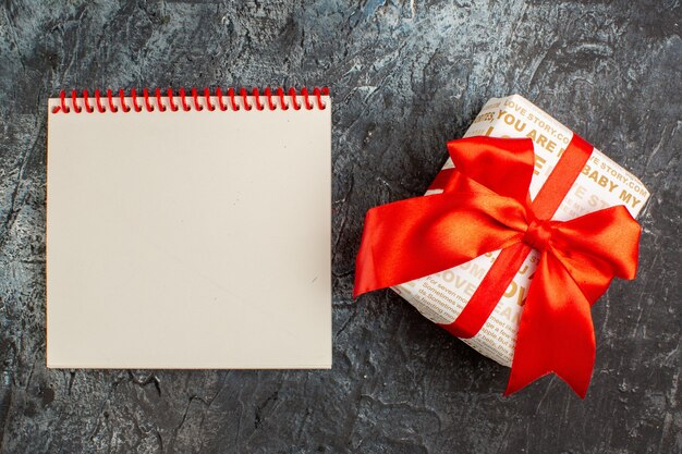 Top view of beautiful gift box tied with red ribbon and notebook on icy dark background