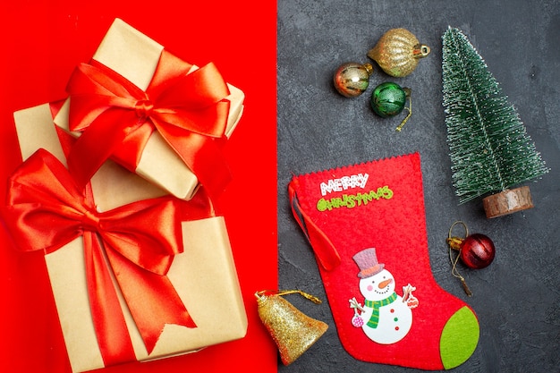 Top view of beautiful gifts with bow-shaped ribbon next to fir branches decoration accessory christmas sock on a red background