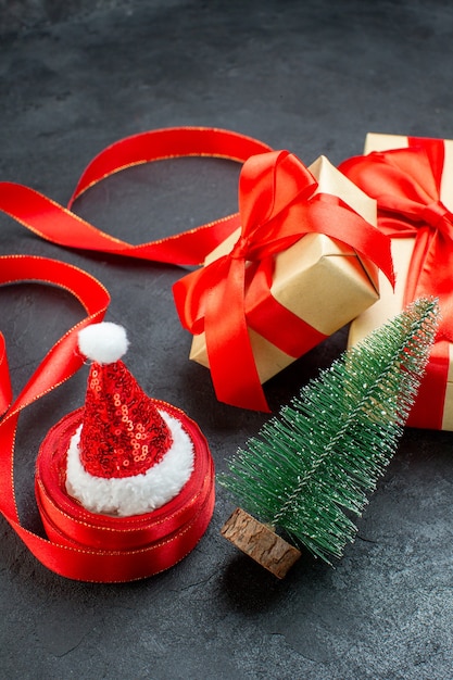 Вид сверху красивых подарков с красной лентой и новогодней елкой в шапке санта-клауса на темном столе