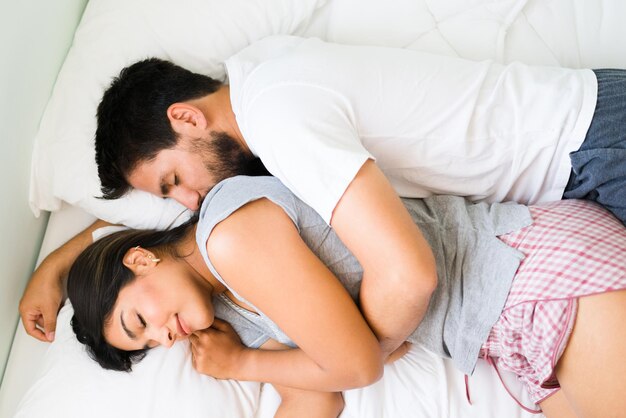 Top view of a beautiful girlfriend and boyfriend sleeping and spooning in bed. Latin couple hugging while falling asleep
