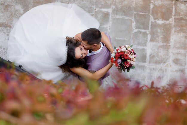 Top view of beautiful wedding couple with wedding bouquet who are kissing outdoors, marriage concept