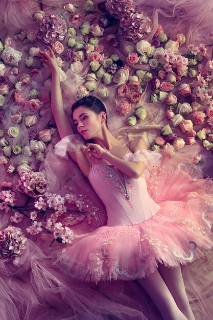 Вид сверху красивой молодой женщины в розовой балетной пачке в окружении цветов